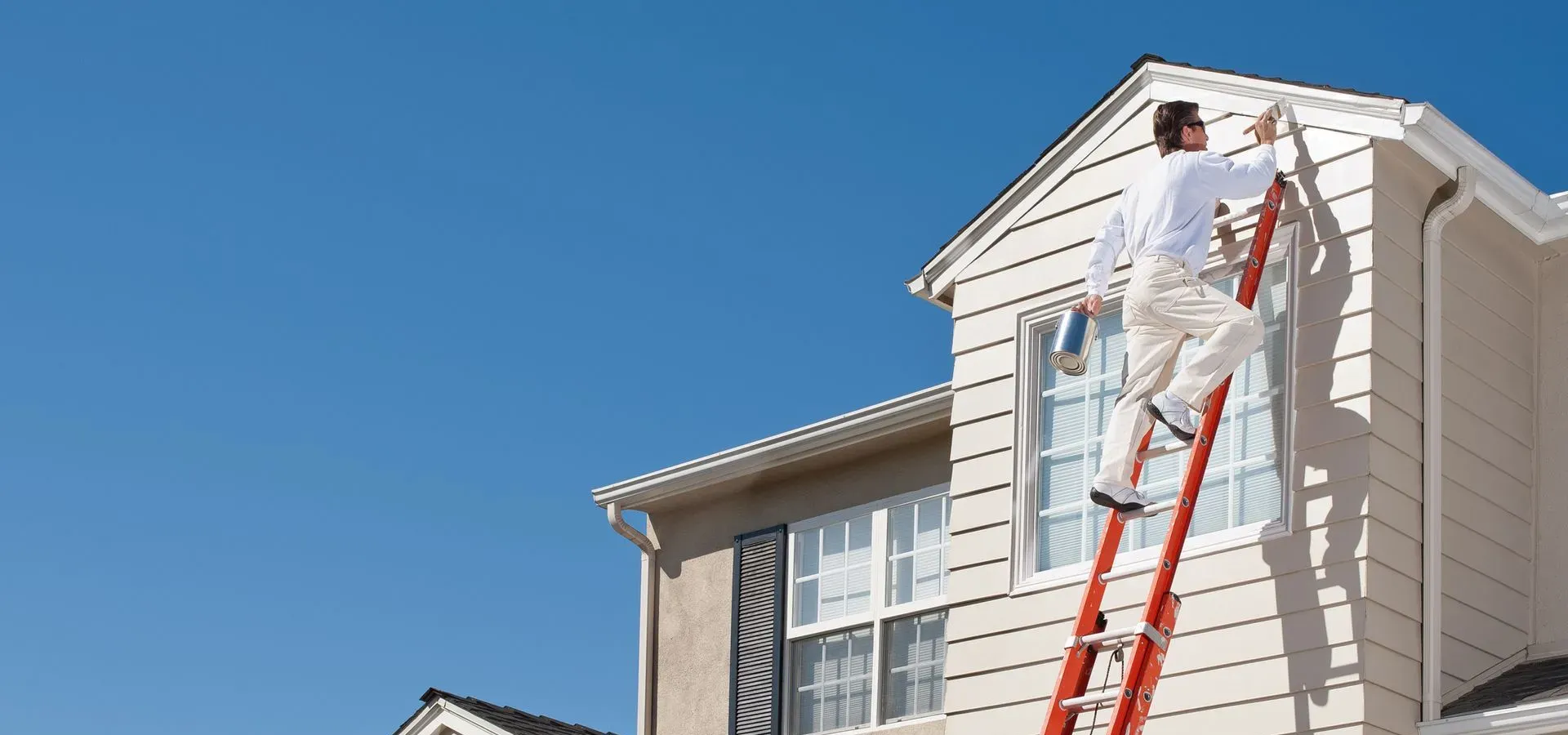 A painter on a tall ladder painting the siding of a two-storey house — exterior house painting in New Bedford, MA