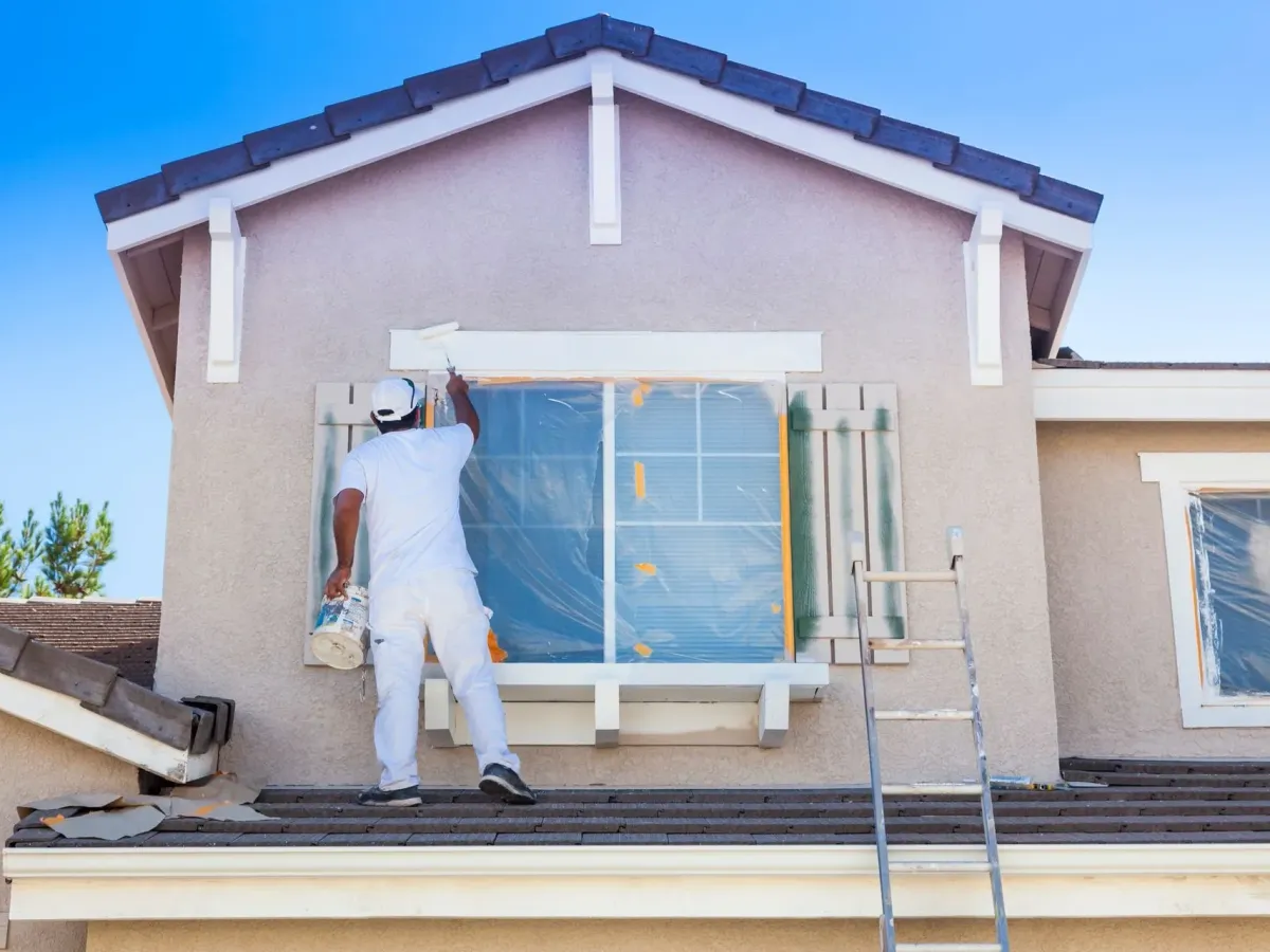 A painter masking a window before painting the outside of a house — prep for exterior painting in New Bedford, MA