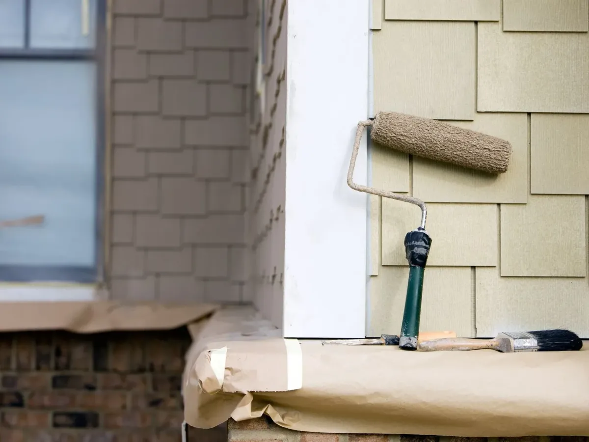 A paint roller resting on shingle siding, drop cloths spread below — house painting in New Bedford, MA
