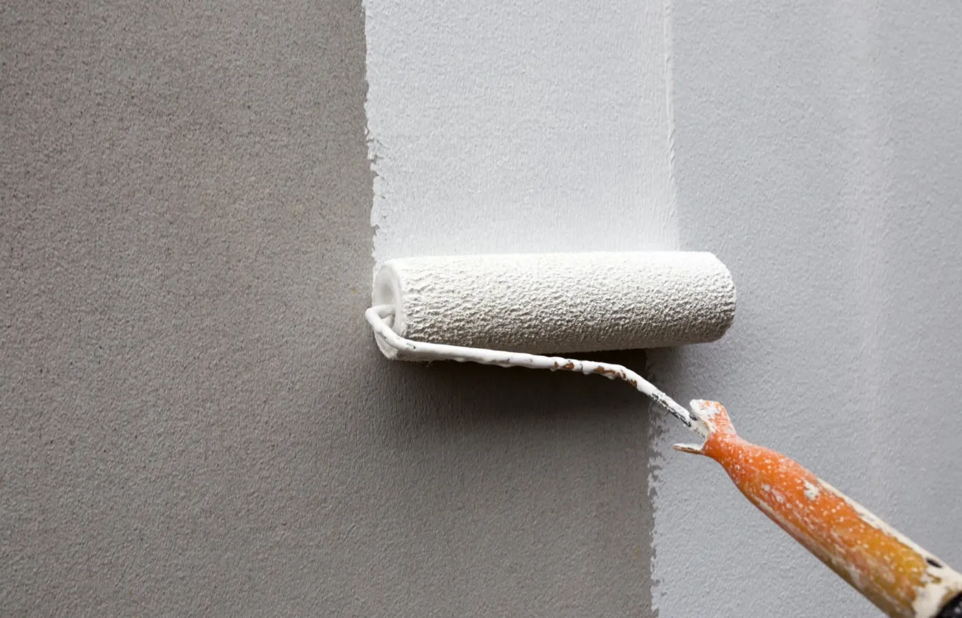 A roller laying fresh white paint over a grey wall — interior painting in New Bedford, MA