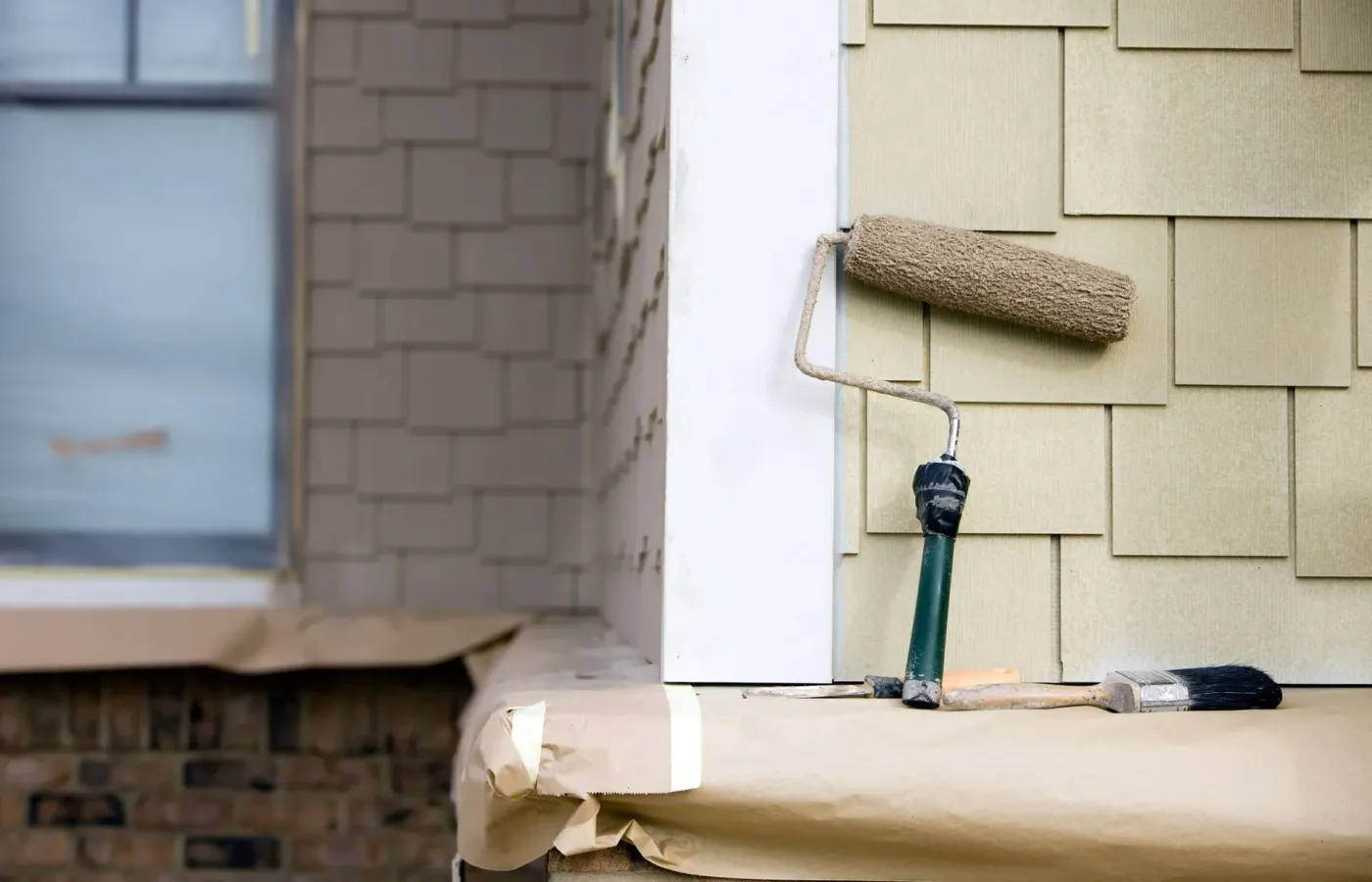 A paint roller resting on shingle siding, drop cloths spread below — exterior painting in New Bedford, MA