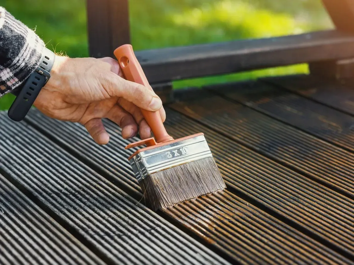 A brush applying dark stain to grey, weathered deck boards — deck restaining in New Bedford, MA