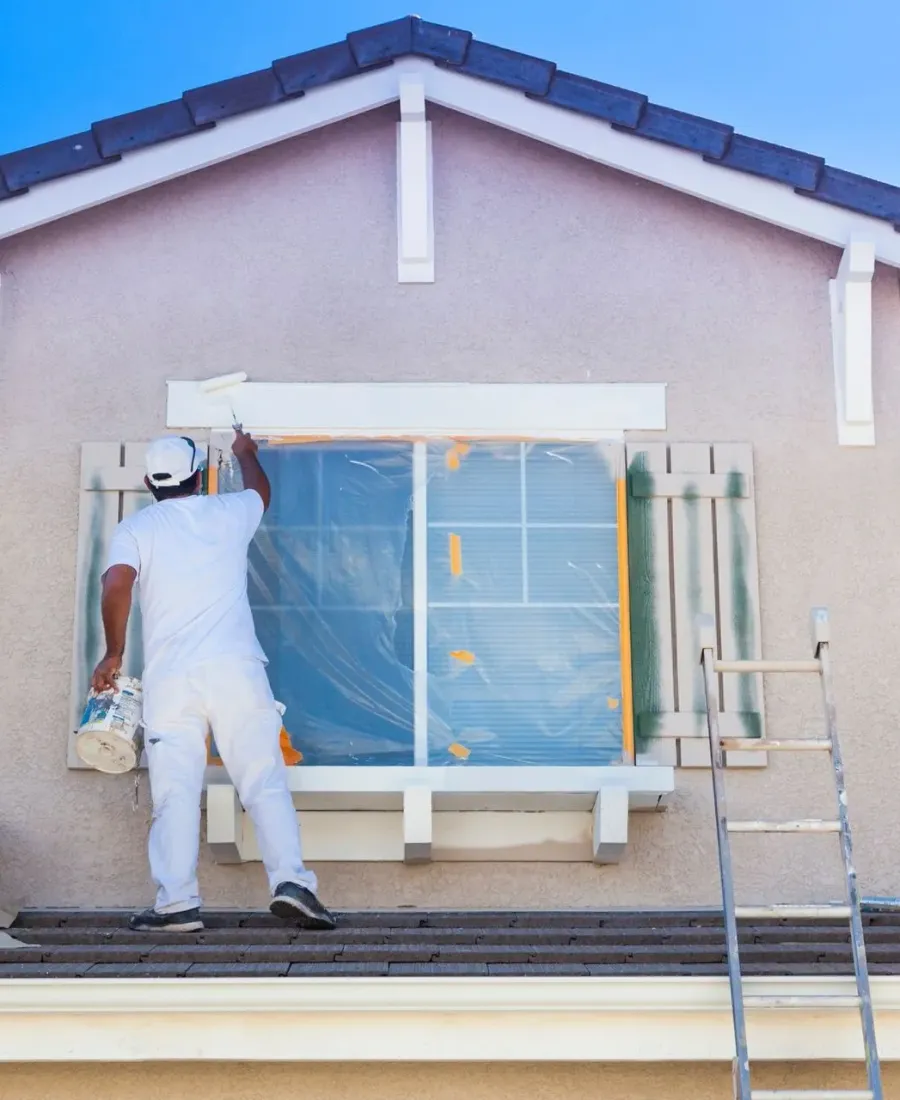 A painter masking a window before painting the outside of a house — exterior painting in New Bedford, MA