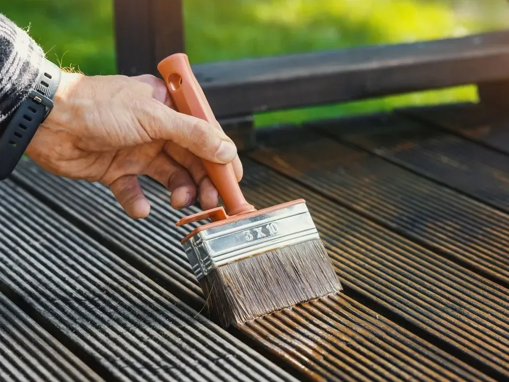 A brush applying dark stain to grey, weathered wooden boards — wood refinishing in New Bedford, MA